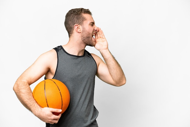 Handsome young man playing basketball over isolated white background shouting with mouth wide open to the side