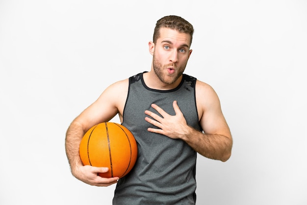 Handsome young man playing basketball over isolated white background surprised and shocked while looking right