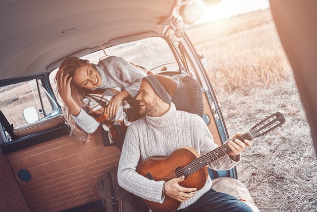 Handsome young man playing guitar for his girlfriend while spending time in motor home