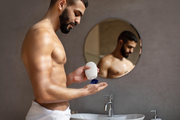 Handsome young man pouring shampoo on palm