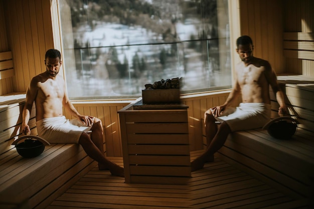 Handsome young man pouring water onto hot stone in the sauna