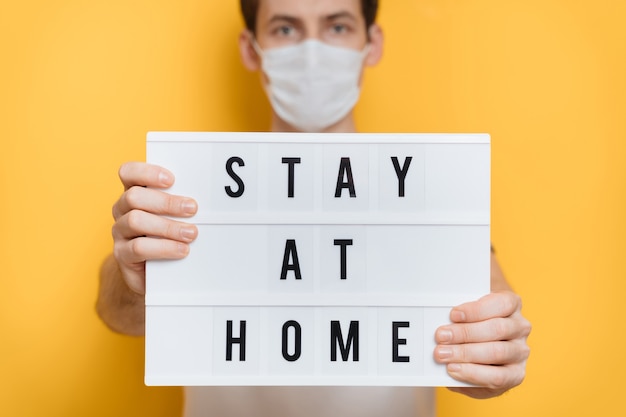 Handsome young man in protective mask holding Stay home sign asking for self isolation and social distancing because of coronavirus outbreak