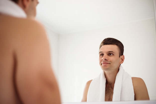 Handsome young man shaving his beard in the bathroom. Portrait of a stylish naked bearded man examining his face in-home mirror.