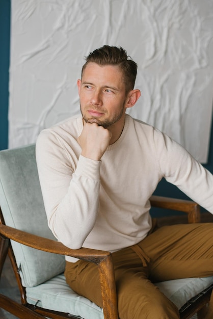 Handsome young man sitting in armchair indoors