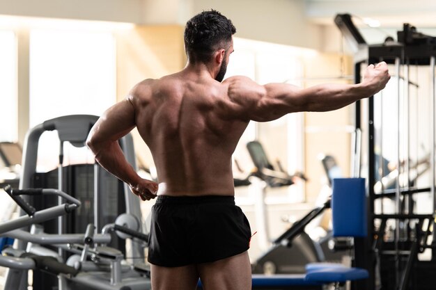 Handsome Young Man Standing Strong In The Gym And Flexing Muscles Muscular Athletic Bodybuilder Fitness Model Posing After Exercises