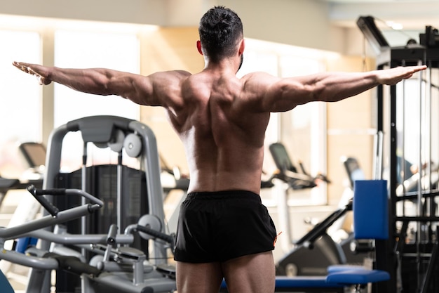 Handsome Young Man Standing Strong In The Gym And Flexing Muscles Muscular Athletic Bodybuilder Fitness Model Posing After Exercises