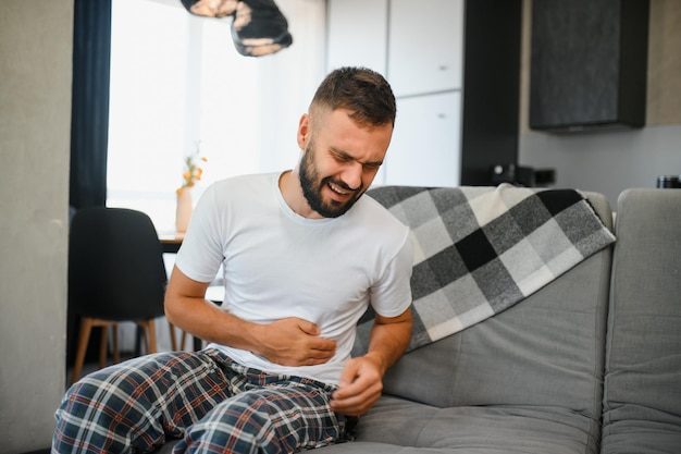 Photo handsome young man suffering from stomach ache while lying on sofa at home