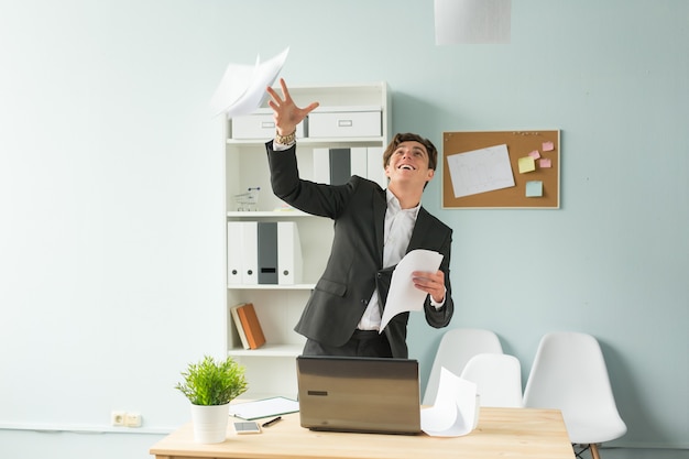 Handsome and young man in suit throws up sheets of paper in office