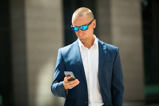 handsome young man in a summer suit on a walk in sunglasses with a phone in his hand