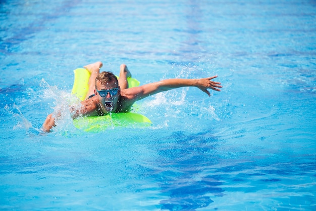 Handsome young man swims on inflatable mattress in blue pool