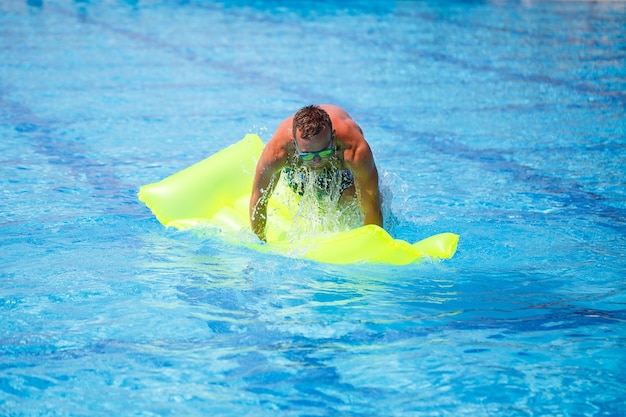 Handsome young man swims on inflatable mattress in blue pool