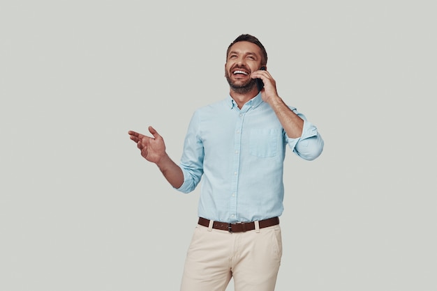 Handsome young man talking on the phone and smiling while standing against grey background