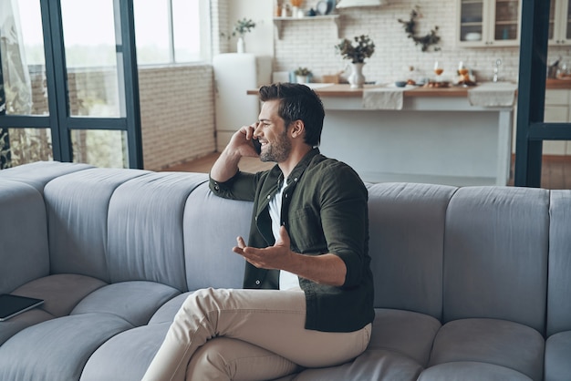 Handsome young man talking on smart phone and smiling while sitting on the sofa