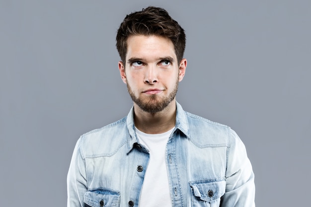 Handsome young man thinking over gray background.