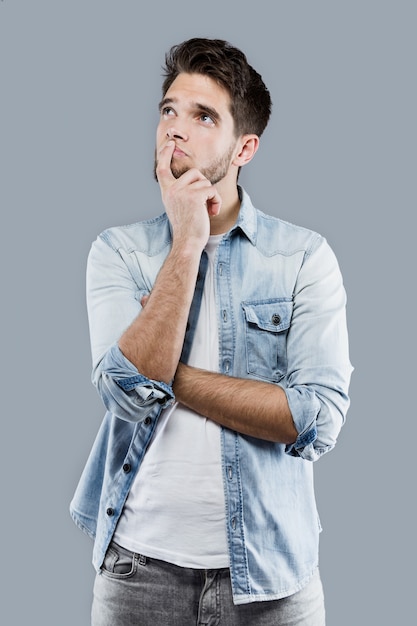 Handsome young man thinking over gray background.