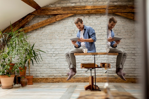 Handsome young man using digital tablet while sitting in the rustic room