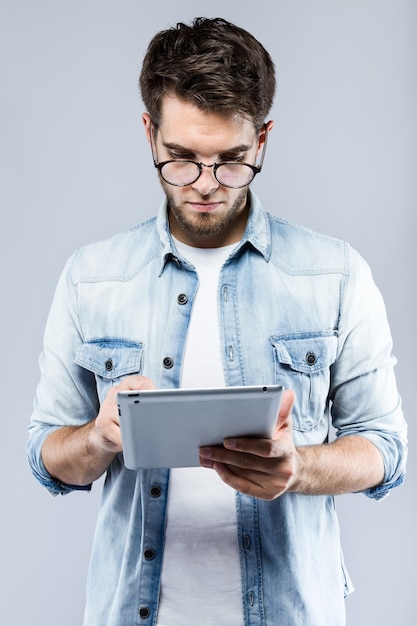 Handsome young man using his digital tablet over gray background.