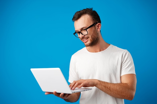 Handsome young man using his laptop against blue background