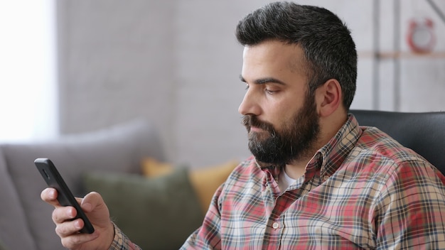 Handsome young man using smartphone sitting at home.