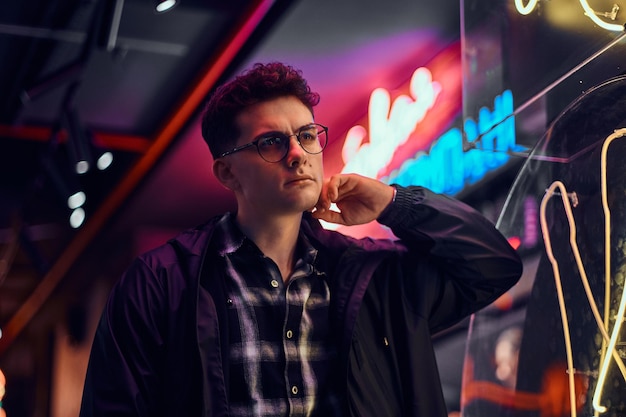 A handsome young man wearing sports hoodie standing in the street at night. Illuminated signboards, neon, lights.