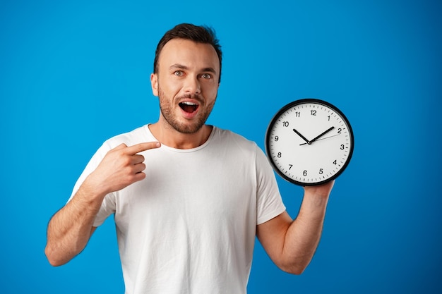 Handsome young man in white tshirt posing with clock against blue background