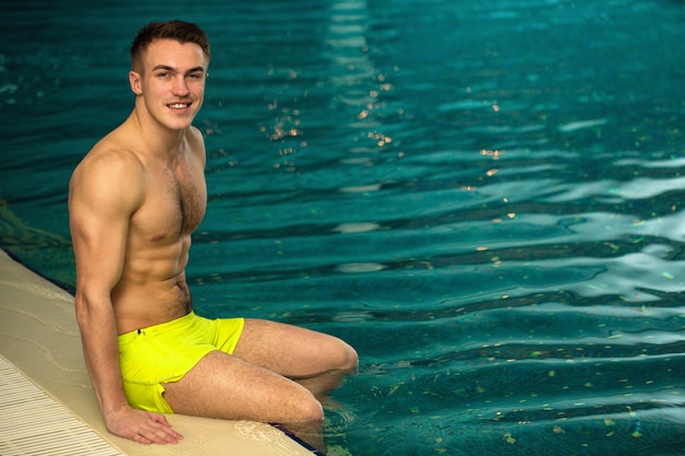 Handsome young man with athletic toned body resting by the swimming pool