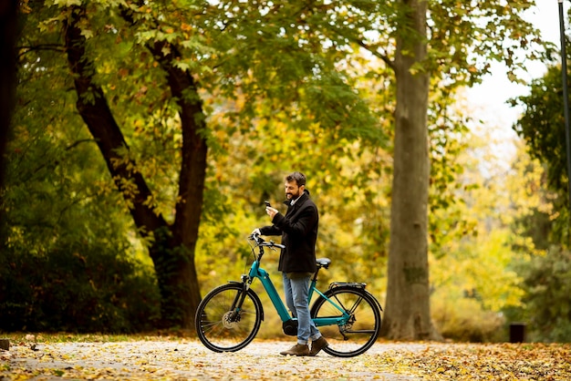 Handsome young man with electric bicycle in the autumn park