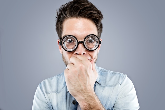 Handsome young man with funny glasses joking and making funny face over gray background.