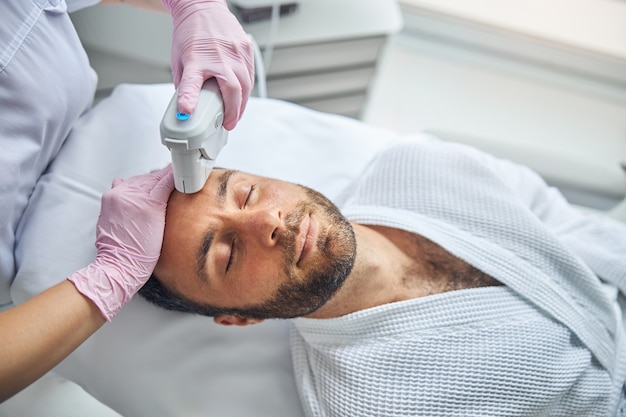 Handsome young man with stubble receiving laser facial treatment in wellness clinic