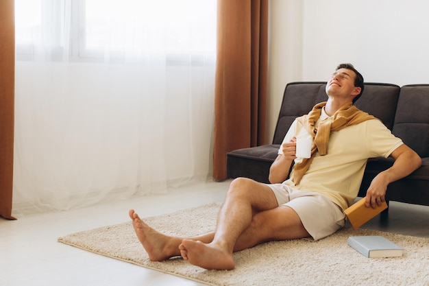 Handsome young man in yellow casual clothes sitting at home reading books and drinking coffee