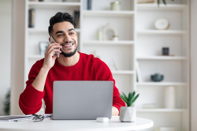 Handsome young middle eastern male talking on mobile phone at home office