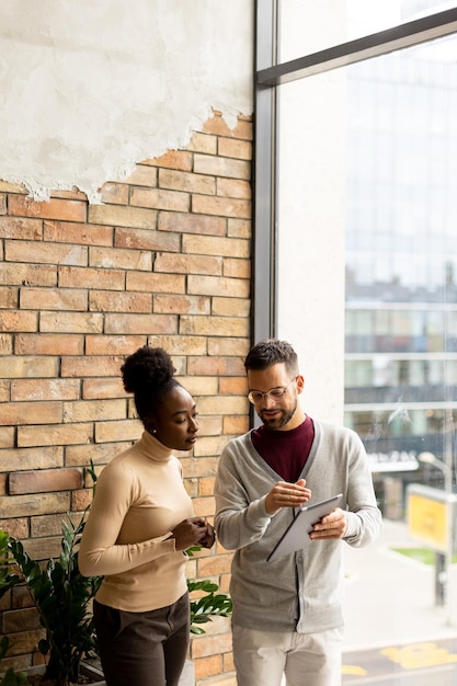 Handsome young multiethnic business couple with digital tablet standing and discussing in the modern office