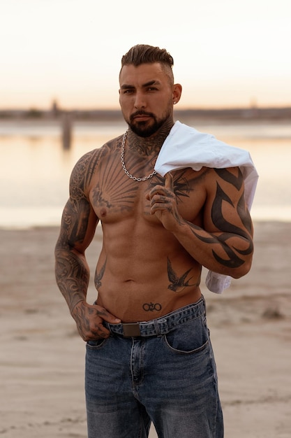 Handsome young muscular italian man posing shirtless on the beach sunset summer time