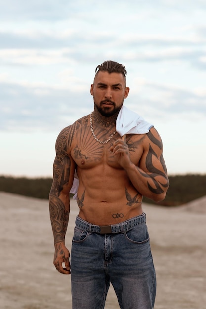 Handsome young muscular italian man posing shirtless on the beach sunset summer time