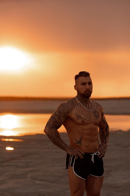 Handsome young muscular italian man posing shirtless on the beach sunset summer time