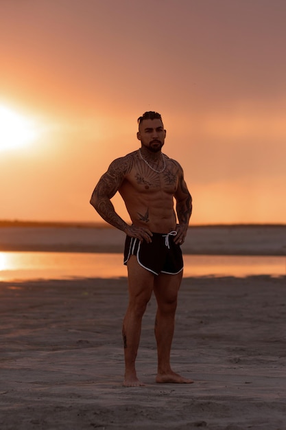 Handsome young muscular italian man posing shirtless on the beach sunset summer time