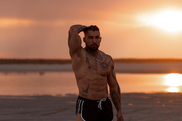 Handsome young muscular italian man posing shirtless on the beach sunset summer time