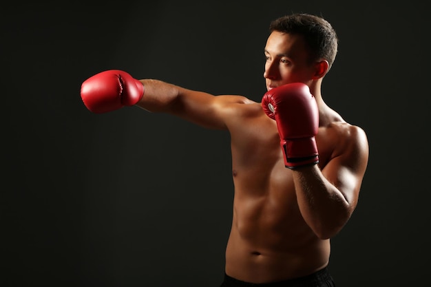 Handsome young muscular sportsman with boxing gloves on dark background