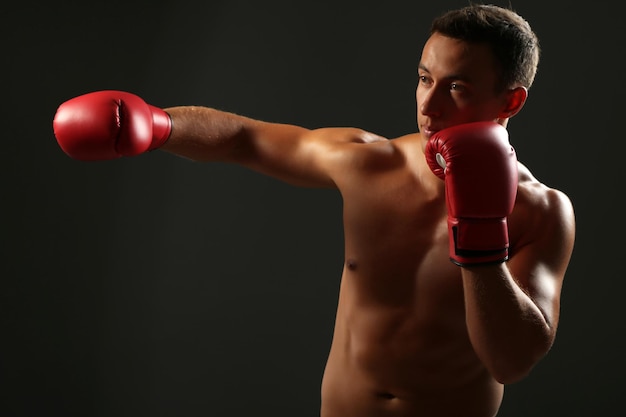 Handsome young muscular sportsman with boxing gloves on dark background