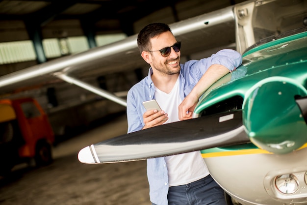 Handsome young pilot checking airplane in the hangar and using mobile phone