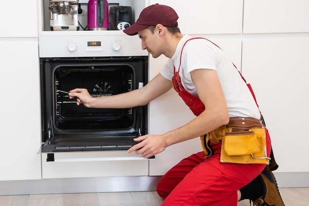 Photo handsome young repairman fixing oven with screwdriver.