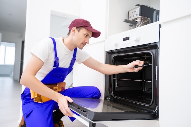 Photo handsome young repairman fixing oven with screwdriver.