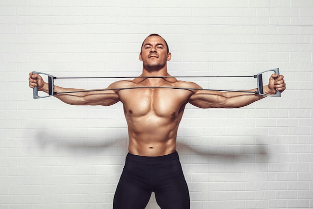 Handsome young sportsman exercising using expander while standing against white background