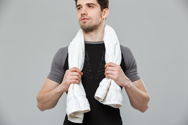 Handsome young sportsman holding towel looking aside.