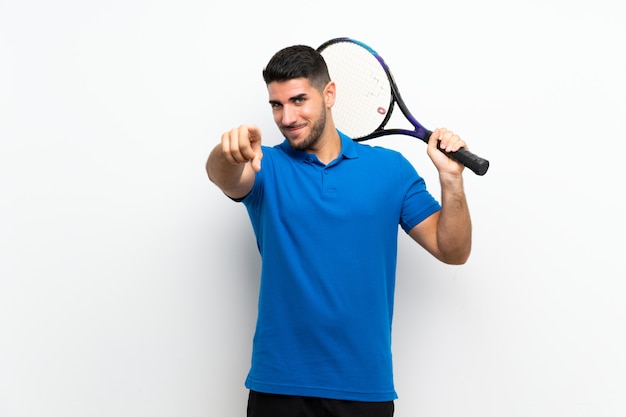 Handsome young tennis player man over white wall points finger at you with a confident expression