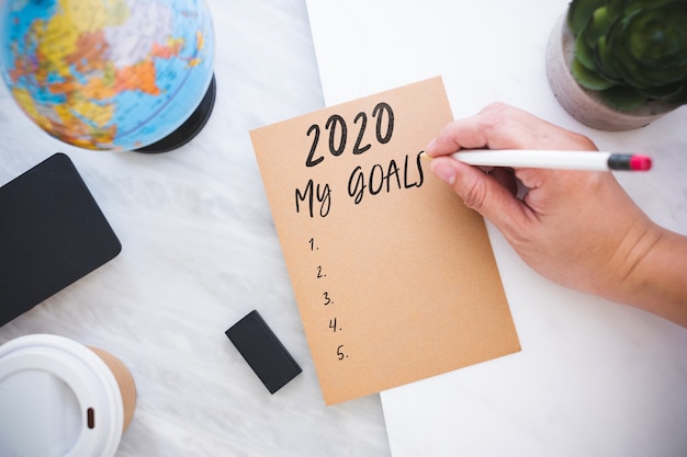 Handwriting 2020 my Goals on brown paper with blue globe, blackboard, coffee cup on marble table