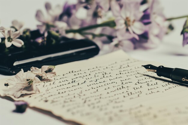 Photo handwritten letter with vintage pen surrounded by fresh flowers on a rustic table