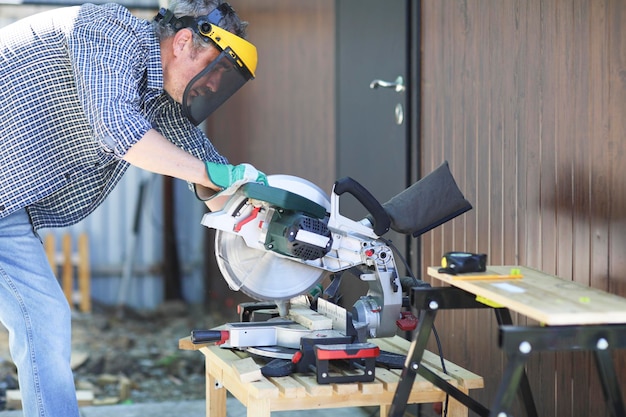 A handyman in a protective helmet works with a miter saw