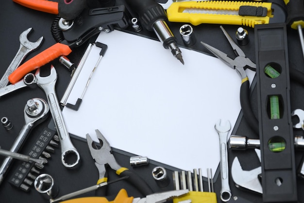 Handyman tool kit on black wooden table with copy space in blank paper tablet Many wrenches and screwdrivers pilers and other tools for any types of repair or construction works