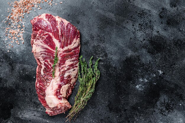 Hanger or onglet raw beef meat steak on butcher table with herbs. Black background. Top View. Copy space.